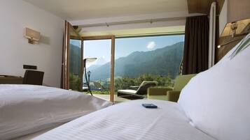 Habitación de hotel con dos camas, un balcón con una silla y vistas a las montañas.