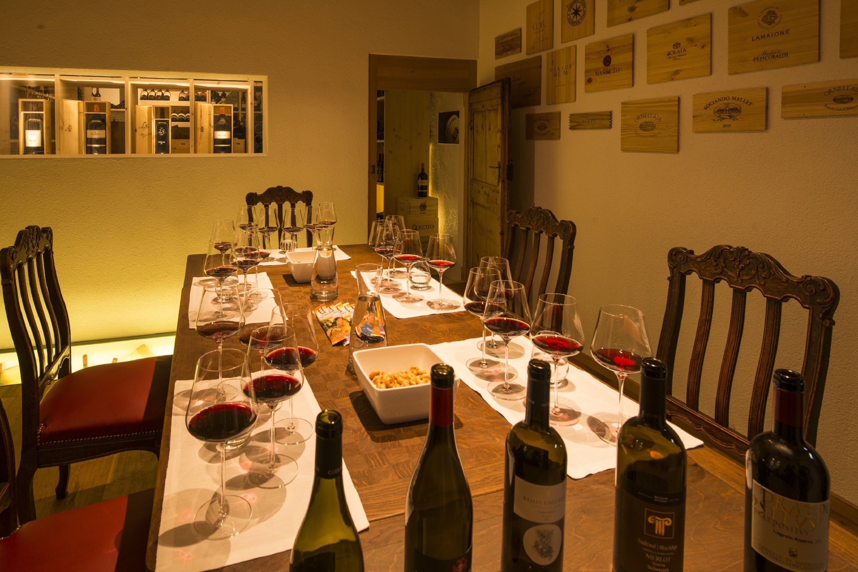 Una mesa de comedor preparada con copas de vino, botellas y un bol de aperitivos.