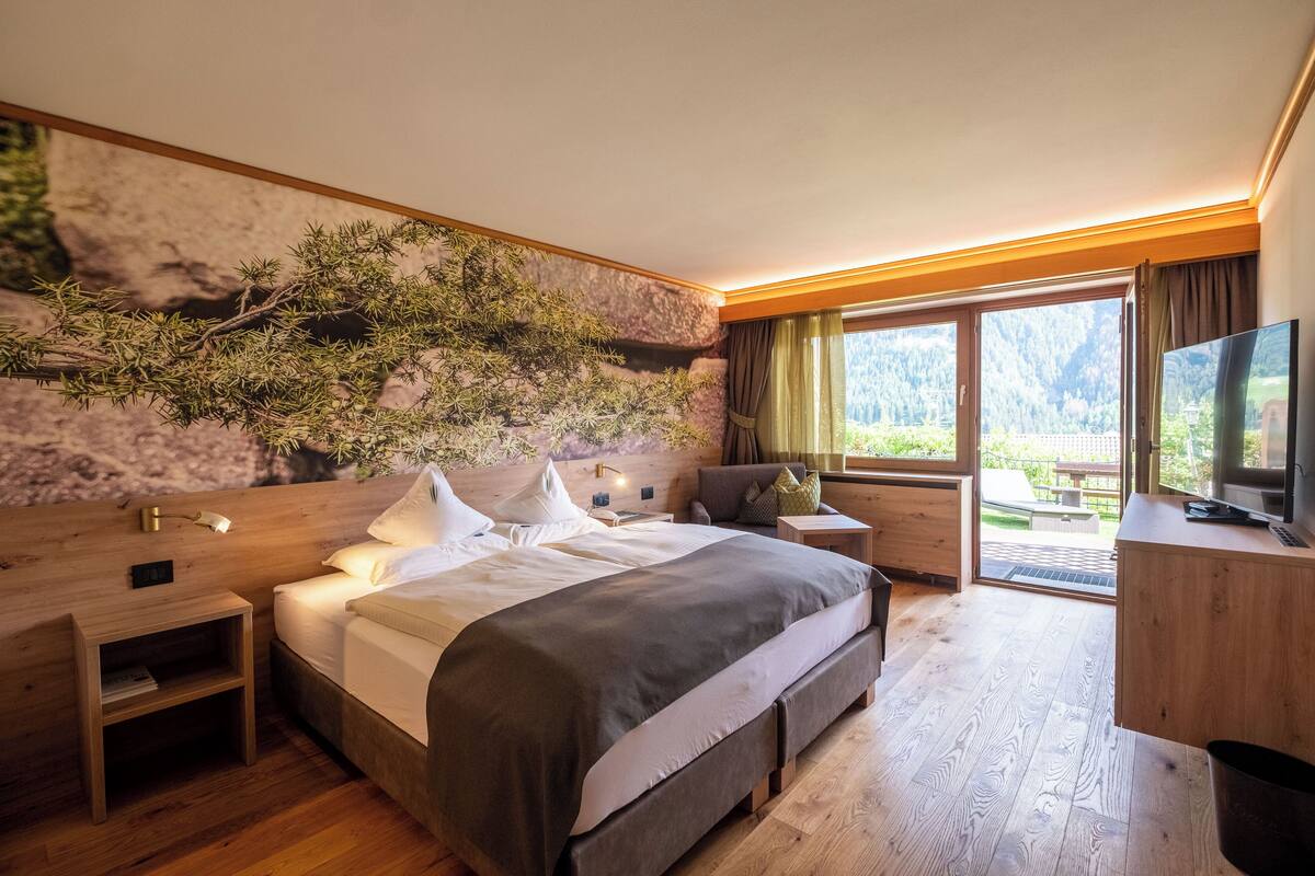A modern bedroom with a large bed, wooden headboard, a nightstand, a desk, and a TV.