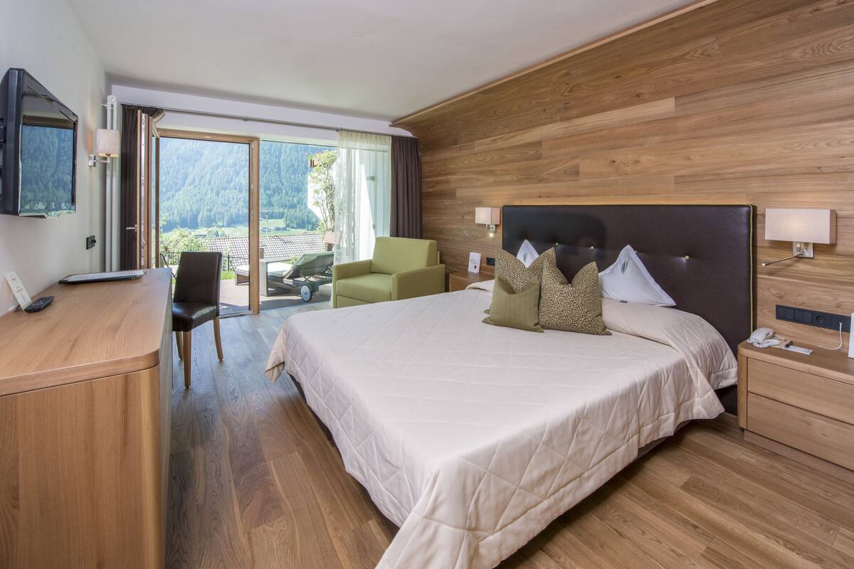 A hotel room with a large bed, a desk, a chair, and a view of the outdoors.