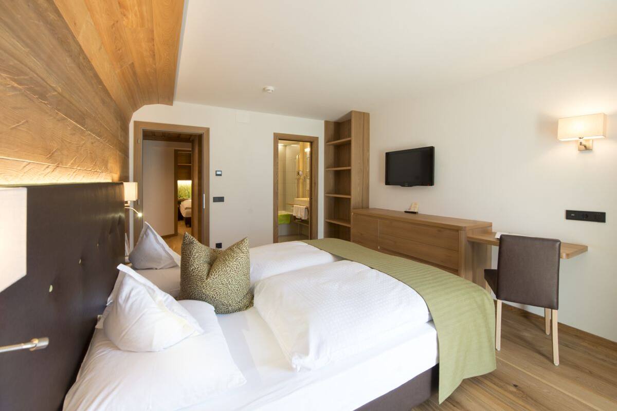 A bedroom with a large bed, a desk, a chair, a TV, and a wardrobe.