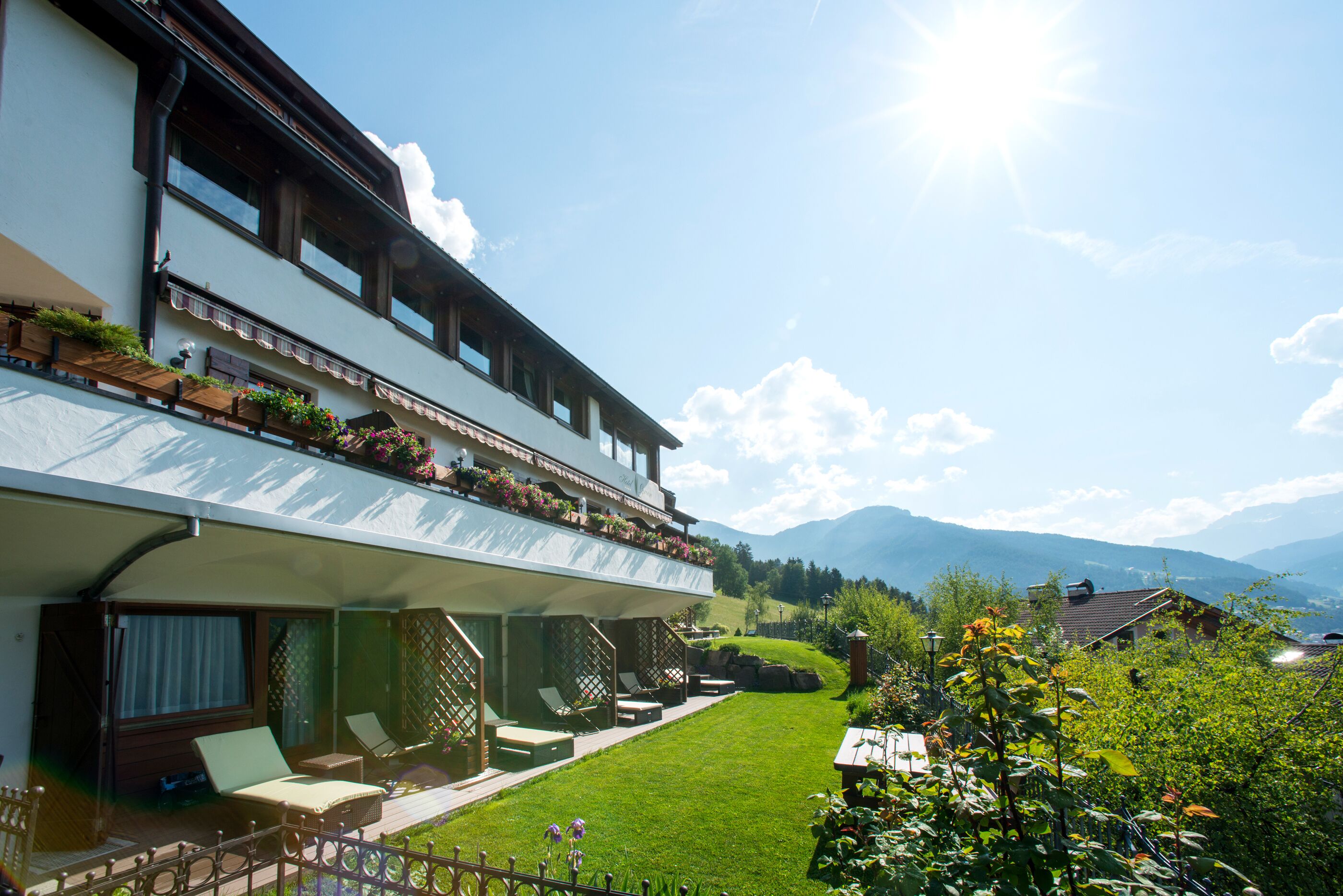 A two-story building with a balcony, a lawn, and mountains in the background.