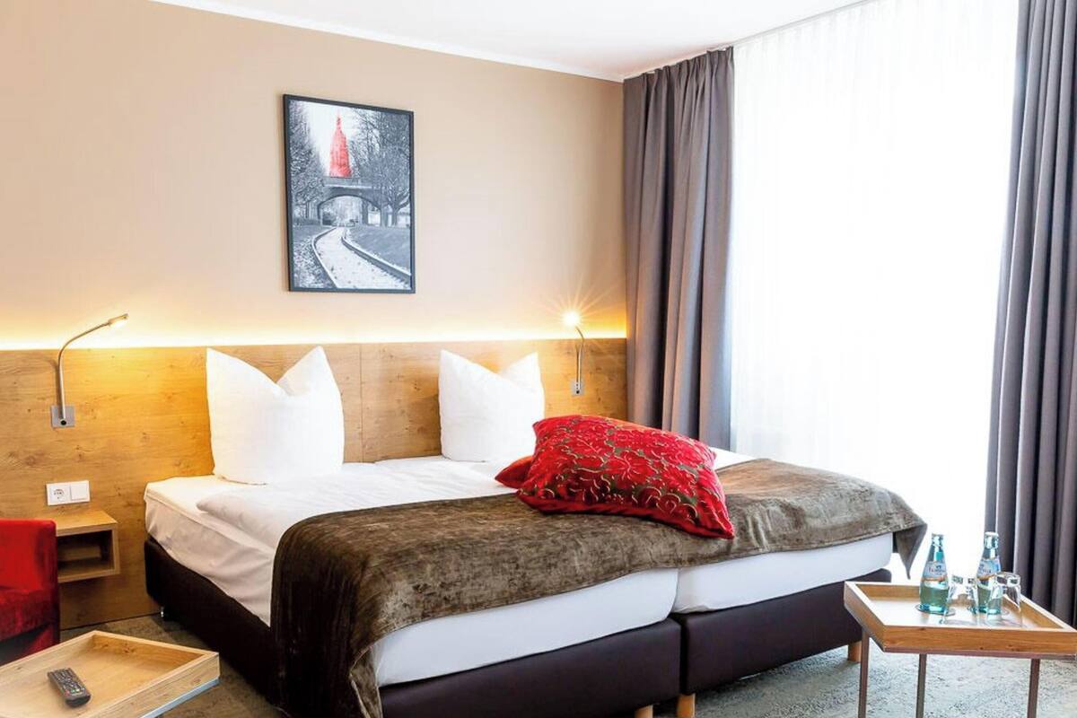 Hotelkamer met een bed, een rode stoel, een nachtkastje met dienblad, en een aan de muur hangend schilderij.