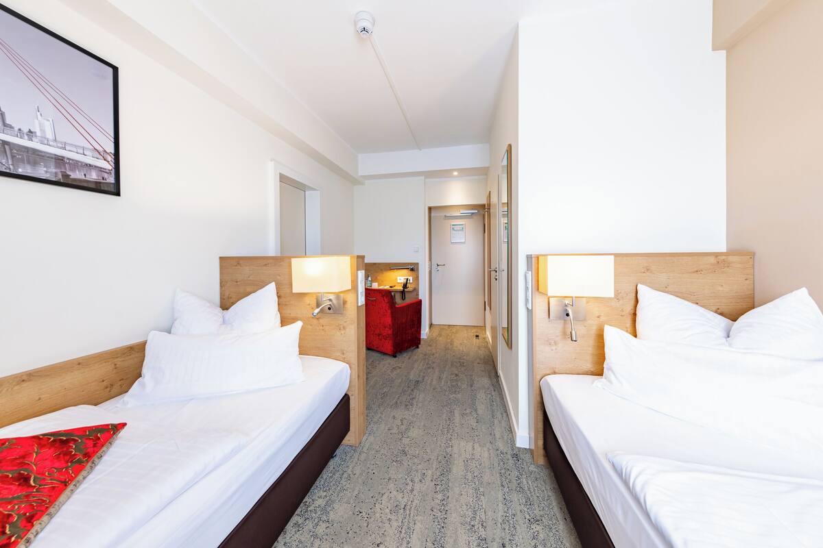 Een hotelkamer met twee bedden, een rode stoel, een bureau en een ingelijst schilderij aan de muur.