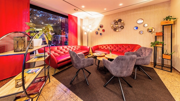 Een moderne loungeruimte met rode leren banken, grijze fauteuils en een houten salontafel.