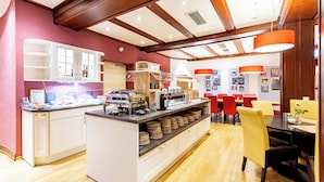 Een moderne keuken met witte kastjes, een centraal eiland met etenswaren, en een eetgedeelte met rode stoelen en gele tafels.