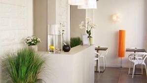 Un espace d’accueil moderne avec un comptoir de réception blanc, une plante en pot et un coin salon comprenant des chaises et une table, le tout dans des tons blancs.