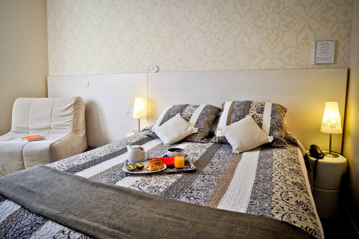 A hotel room with a neatly made bed, a bedside table with a lamp, and a chair.