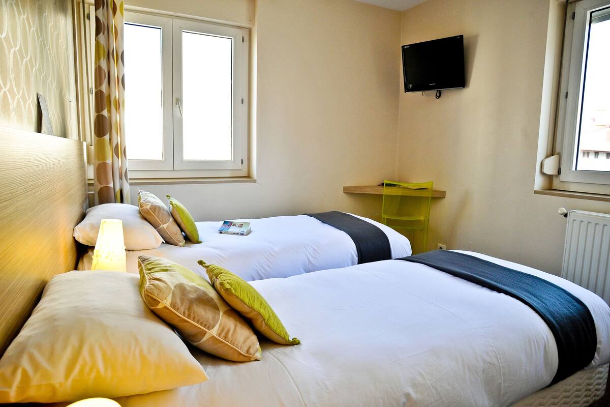 A hotel room with two beds, a TV on the wall, and a window with curtains.
