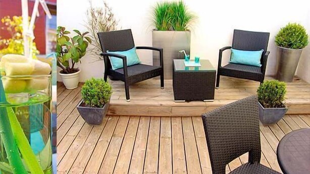 Une terrasse en bois avec deux chaises en osier noir, une petite table et des plantes en pot.