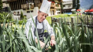 Un chef con gorro blanco y delantal a rayas trabaja con cebollines en un jardín.