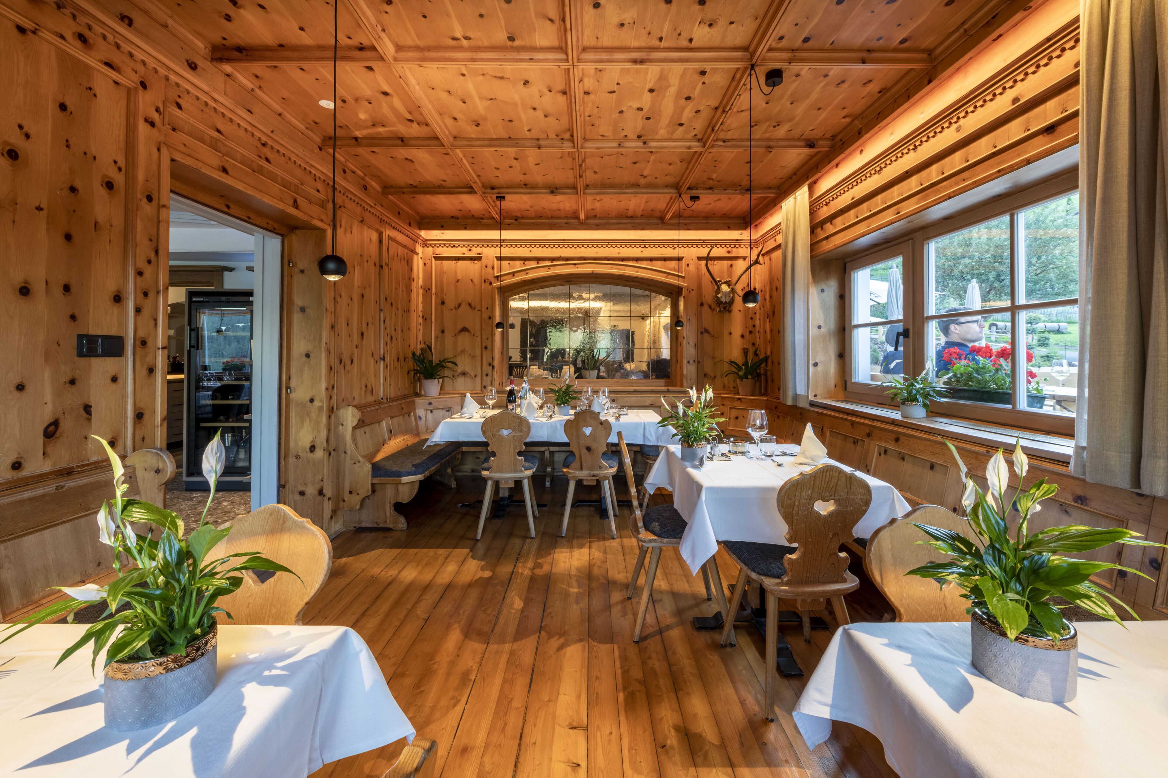 A wooden interior with tables and chairs, potted plants, and a large window with a view.