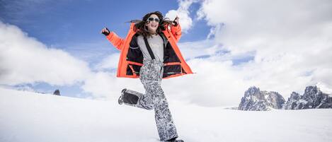 Een persoon snowboardt op een besneeuwde berg, met een heldere lucht en bergen op de achtergrond.