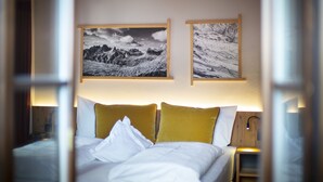 A hotel room with a bed, two pillows, a nightstand, and two framed pictures on the wall. -  Hotel Platz (Castelrotto)