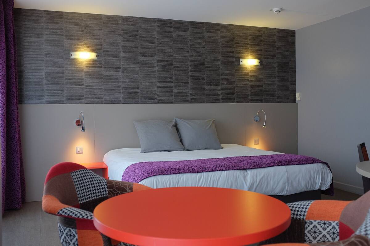 Een hotelkamer met een bed, twee bedlampen, een tafel en stoelen.