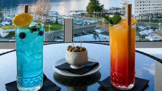 Deux boissons sur une table, avec vue sur un lac et des montagnes.
