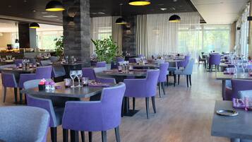 A modern restaurant with purple chairs, black tables, and pendant lighting.