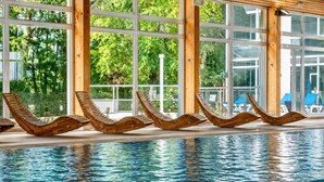 Une piscine intérieure dotée de chaises longues en bois et de grandes fenêtres.