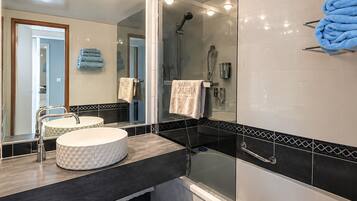 A modern bathroom with a round sink, a glass-enclosed shower, and a towel rack with blue towels.