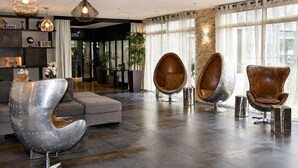 Un hall d’entrée moderne avec un canapé, deux fauteuils en forme d’œuf, une sculpture métallique et des luminaires suspendus.