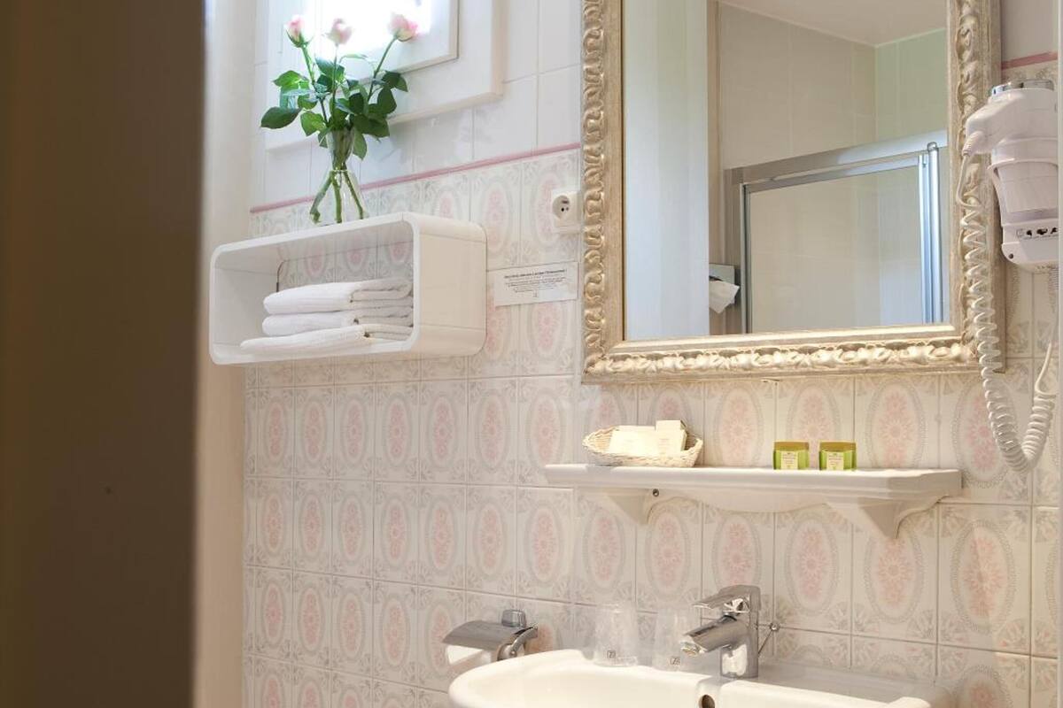 Un baño con un lavamanos blanco, un espejo con un marco decorativo y una repisa con artículos de aseo.