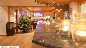 Um hall amplo com teto de madeira, uma árvore de Natal, um balcão de recepção de mármore e uma tela de televisão.