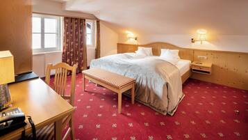 A hotel room with a bed, bedside tables, a desk with a telephone, a chair, and a bench.