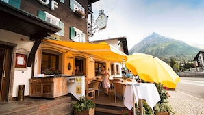 Restaurante com mesas ao ar livre, vista para as montanhas e placa indicando que é um restaurante.