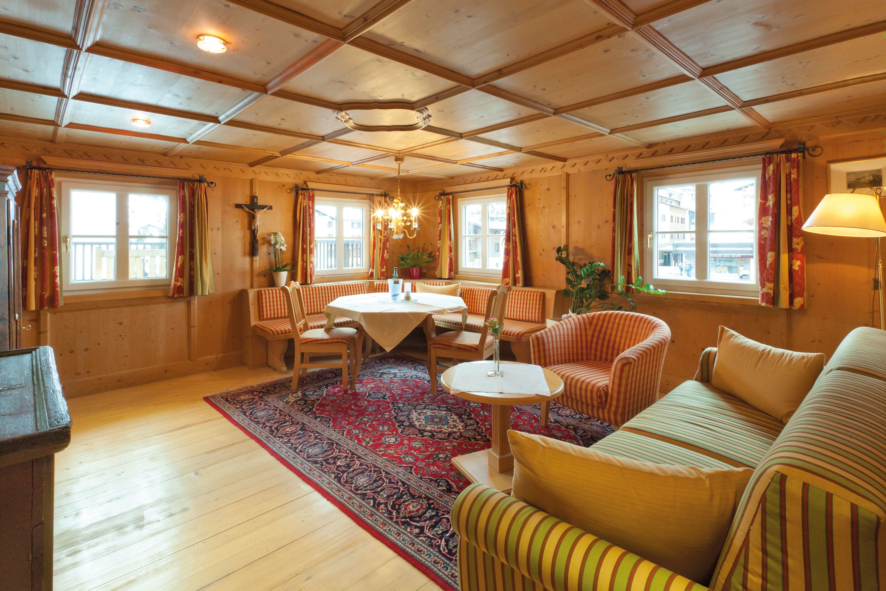 A cozy room with wooden walls, a round table, striped sofas, and a red patterned rug.