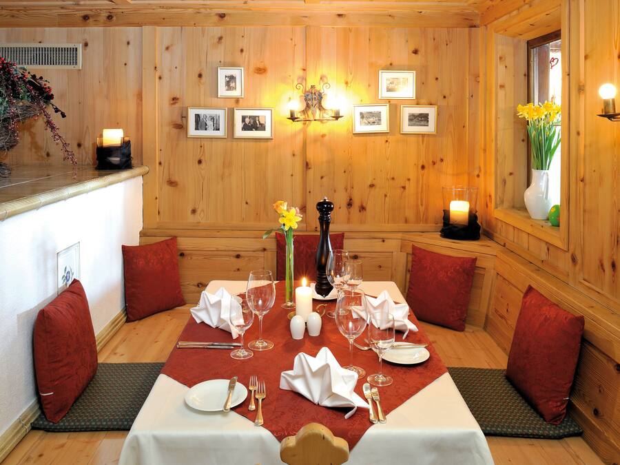 Ein Zimmer mit Holzwänden, ein Tisch für zwei Personen gedeckt, mit roten Kissen, weißer Tischdecke und Kerzen.