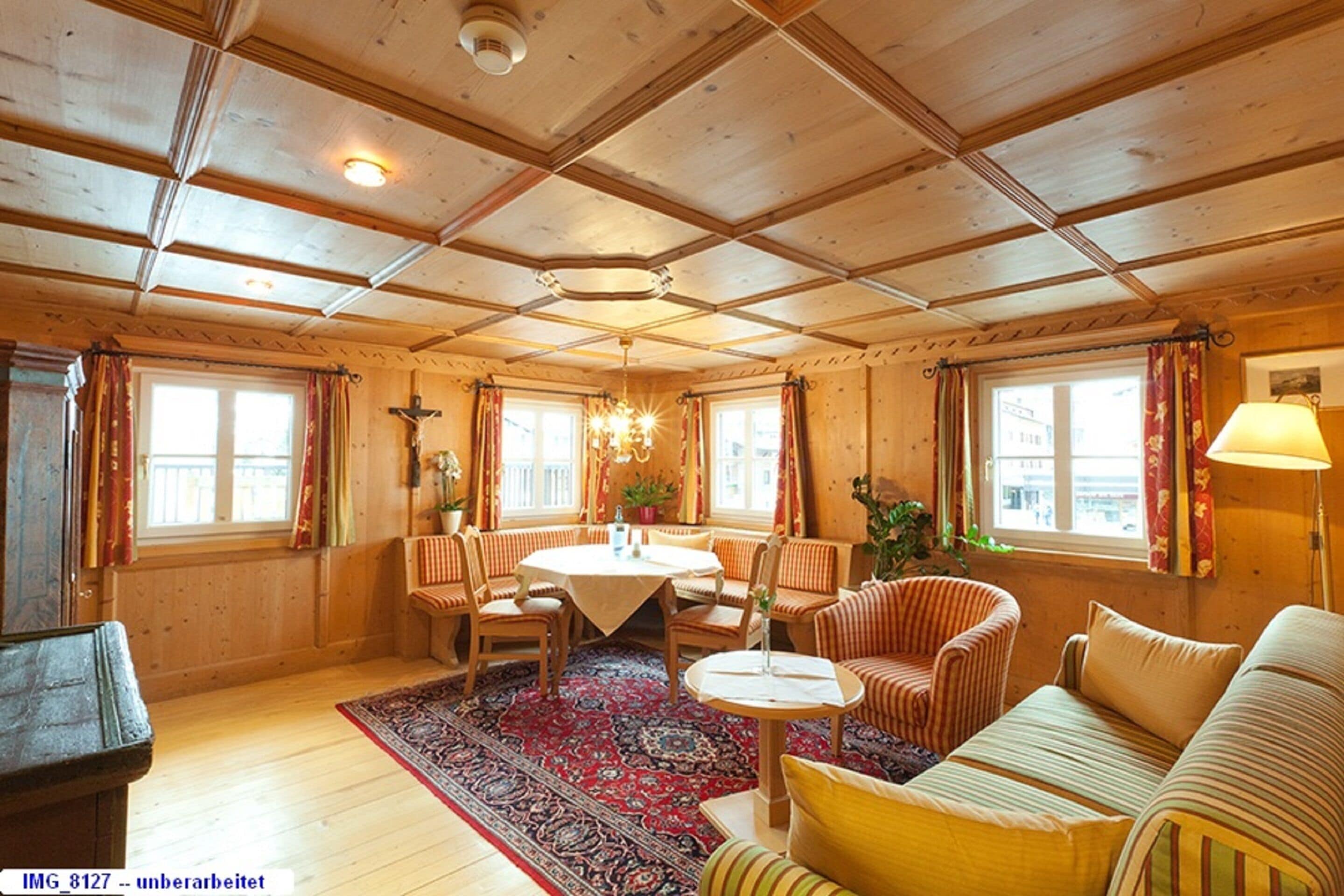 Ett mysigt rum med träväggar och träpanel i taket, ett runt bord med stolar, en soffa och en mönstrad matta.