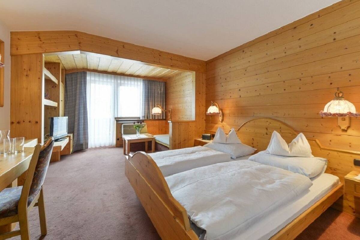 A wooden cabin-style room with two beds, a desk, and a chair.