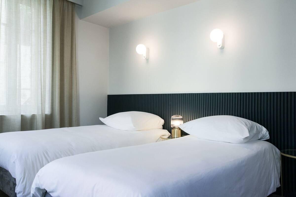 A hotel room with two beds, a dark headboard, and two wall-mounted lights.