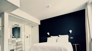 Habitació d'hotel moderna amb un llit gran, un armari encastat, un bany amb dutxa i una paret decorativa fosca.