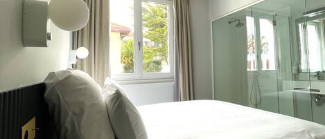 Ein Hotelzimmer mit Bett, einem fensterbepflanzten Fenster, einer Dusche und einer Wandleuchte.
