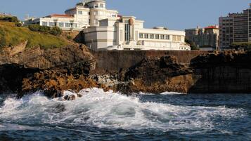 Un hôtel situé sur la côte, avec plusieurs étages, une tour imposante et une plage rocheuse.