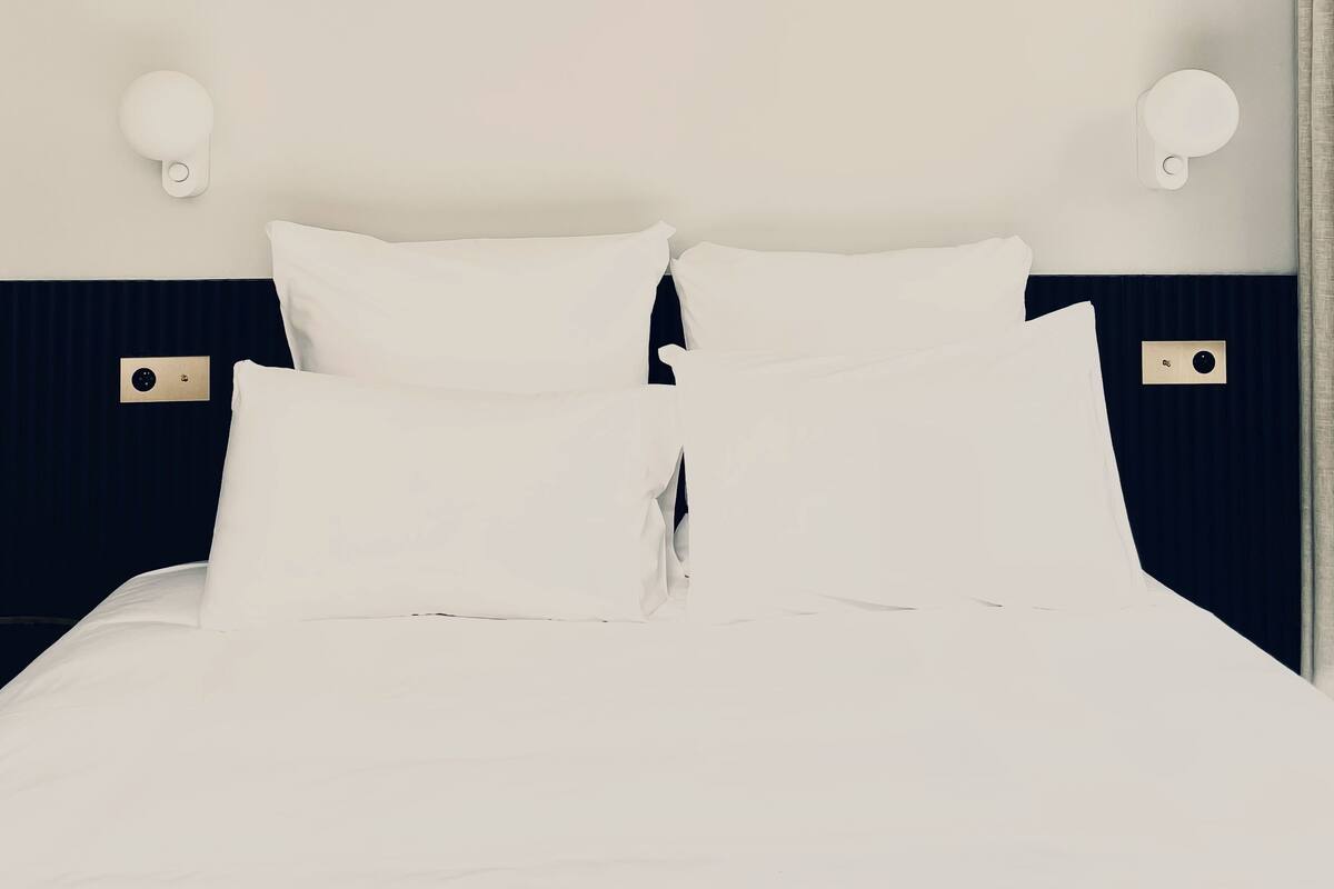 A neatly made bed with white linens and two wall-mounted light fixtures on either side.