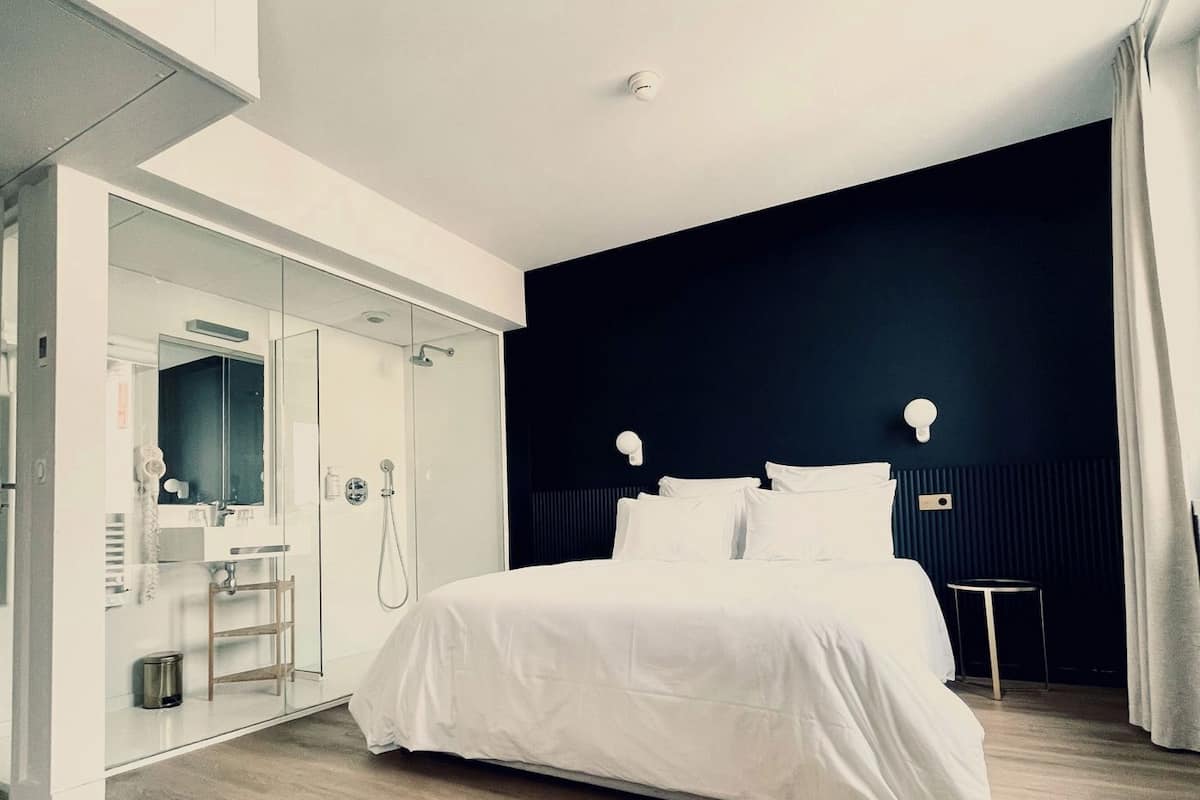 A modern hotel room with a large bed, a glass-enclosed shower area, and a dark accent wall.