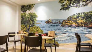 Zona de menjador amb un mural d'una escena costanera, taules de fusta i cadires negres.