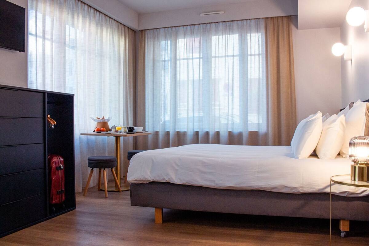A hotel room with a bed, a desk with breakfast items, a wardrobe, and a lamp.