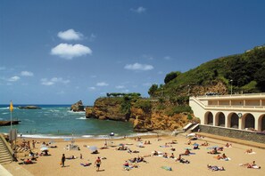A beach with a rocky coastline, a bridge, and a building with arches. - Hotel Le Gamaritz (Biarritz)