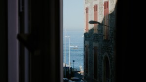 Vista per una porta oberta d'un edifici costaner, amb un fanal i cotxes aparcats.