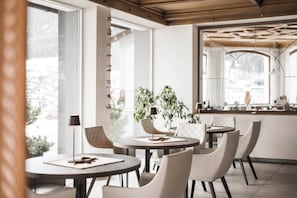 A modern dining area with round tables, white chairs, and potted plants. - Rainell Dolomites Retreat (Castelrotto)