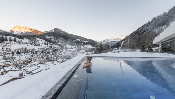 A person in a pool with a view of a snowy mountain town and buildings. - Rainell Dolomites Retreat (Castelrotto)