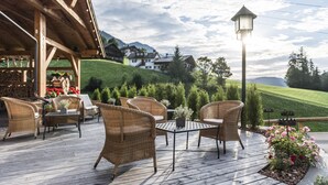 An outdoor patio with wicker furniture and a table, overlooking a green landscape and houses in the background. - Rainell Dolomites Retreat (Castelrotto)