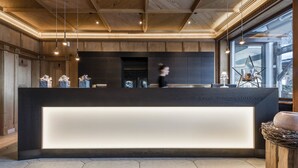 A modern reception desk with a dark wood finish, a glass partition, and a view of the outdoors through large windows. - Rainell Dolomites Retreat (Castelrotto)