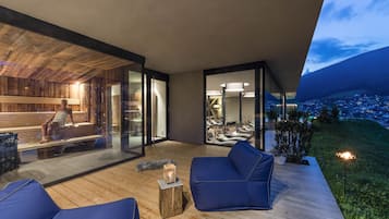 Ein moderner Außenbereich mit Holzterrasse, einer gläsernen Sauna und Blick auf eine Stadtlandschaft im Abenddämmerung.