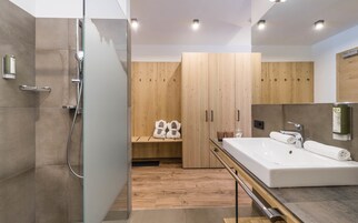 Un baño moderno con cabina de ducha de vidrio, tocador de madera con lavamanos grande y armario de madera con banco.