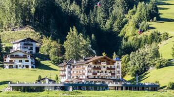 Alpen Hotel Rainell offers stunning mountain views from its balconies, surrounded by dense forest and a cable car system.