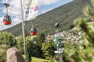 Un sistema de teleférico, un cartel con varios destinos marcados y un pueblo montañoso al fondo.